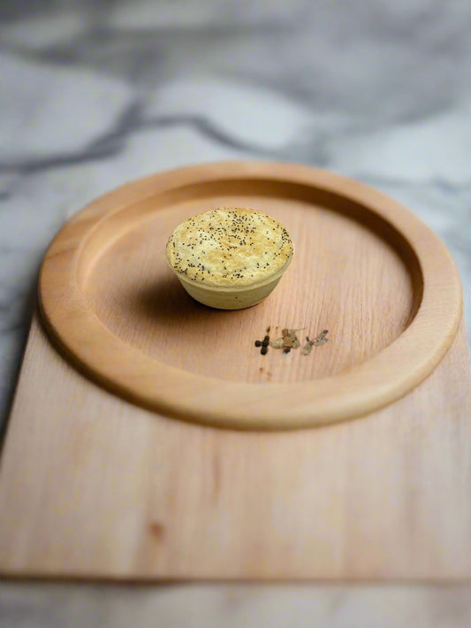 Wooden cutting board with a Single Serve Goat Curry pie on it 